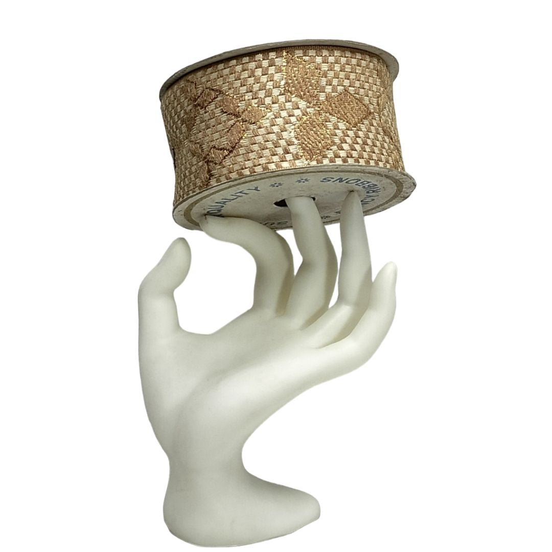 Mannequin hand holding a spool of decorative ribbon on a white background